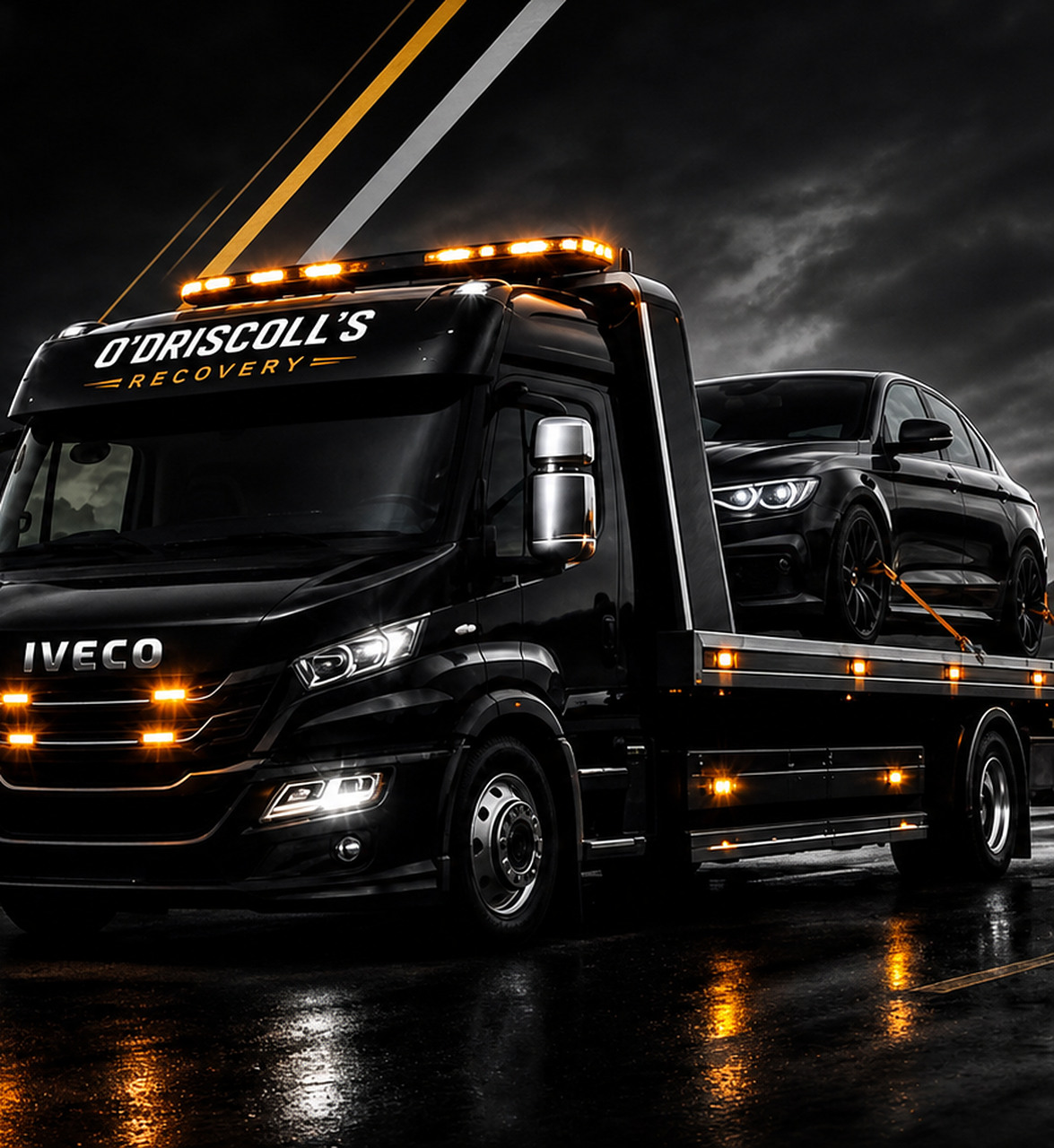O’Driscoll’s Recovery black Iveco recovery truck carrying a black car on a wet road at night